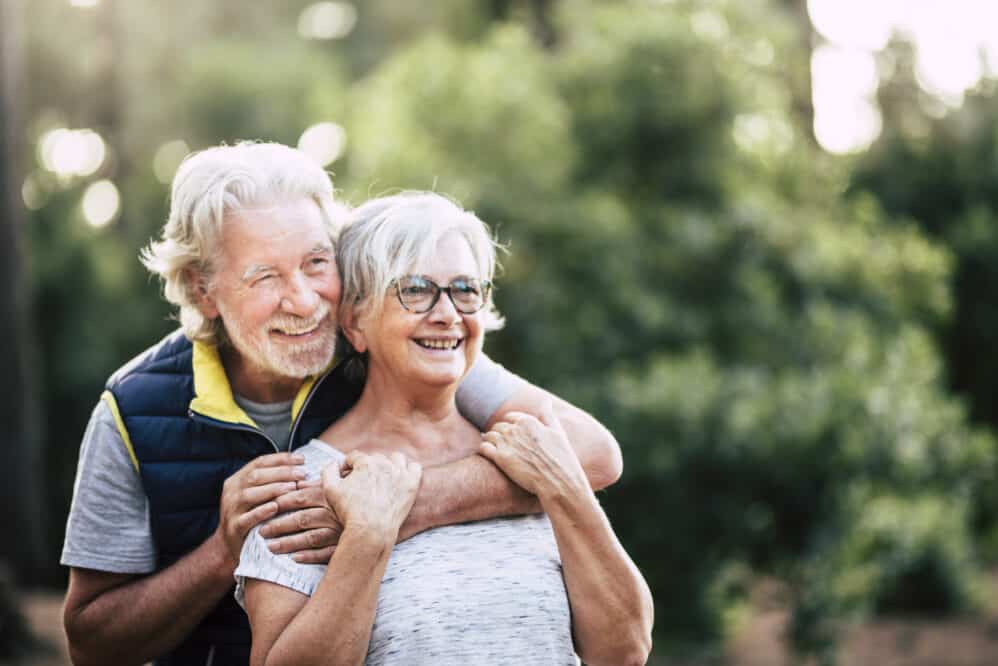 Old mature retired senior people smile and enjoy the love couple during outdoor leisure activity together - green forest and wood in background for environment concept